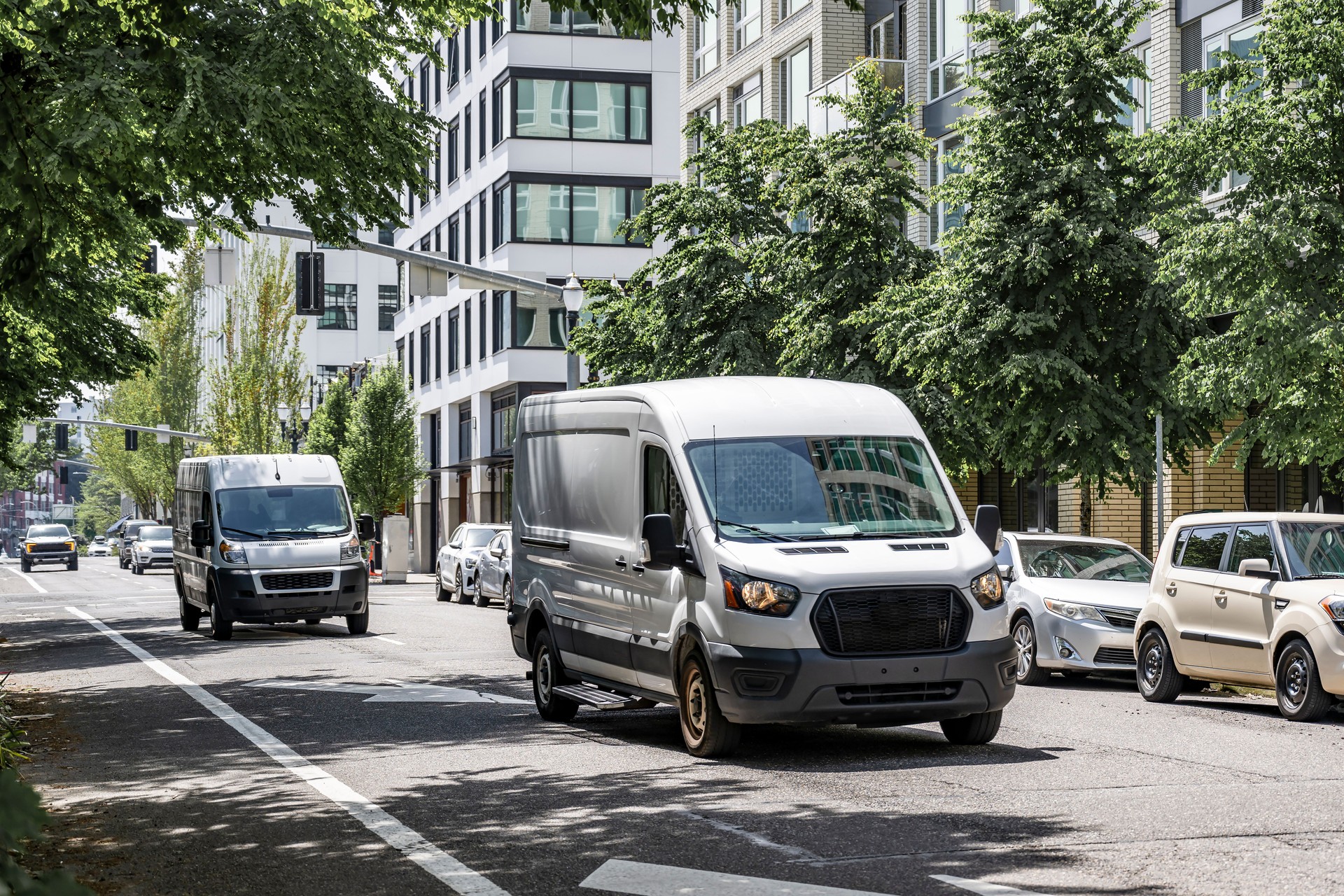 Commercial cargo mini vans making deliveries driving on the urban city street with multilevel apartment buildings